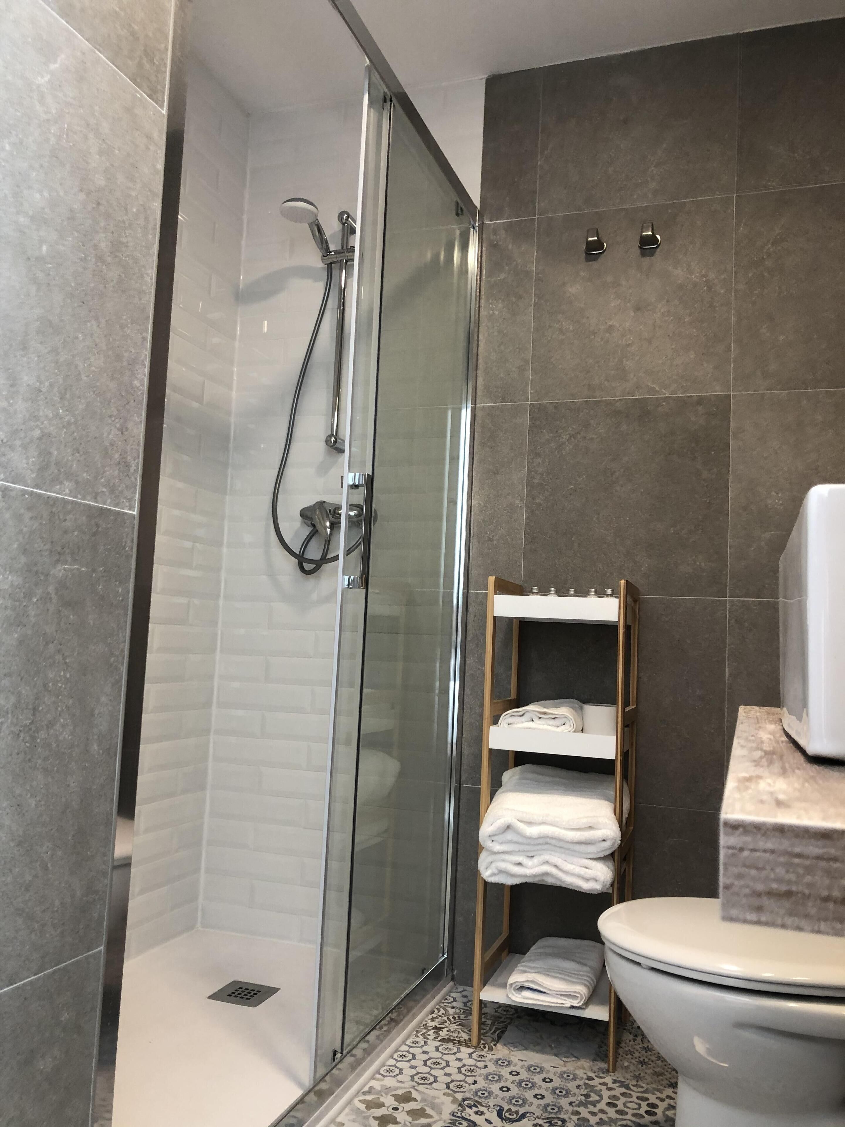 Ein modernes Badezimmer mit einer Glasdusche, einer Toilette und einem Ablagefach mit Handtüchern.