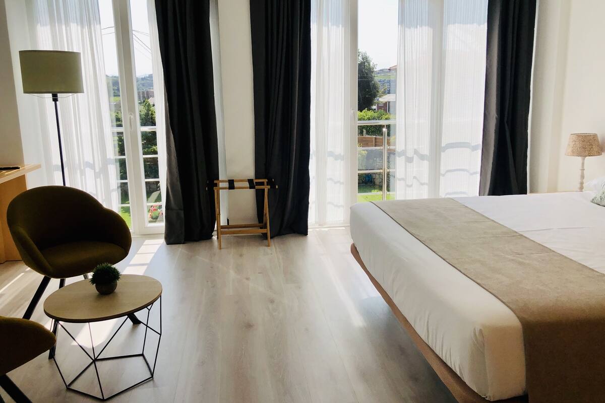 Ett hotellrum med en stor säng, ett litet bord, en stol och utsikt över omgivningarna.