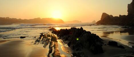 A beach with a rocky outcrop and waves at sunset.