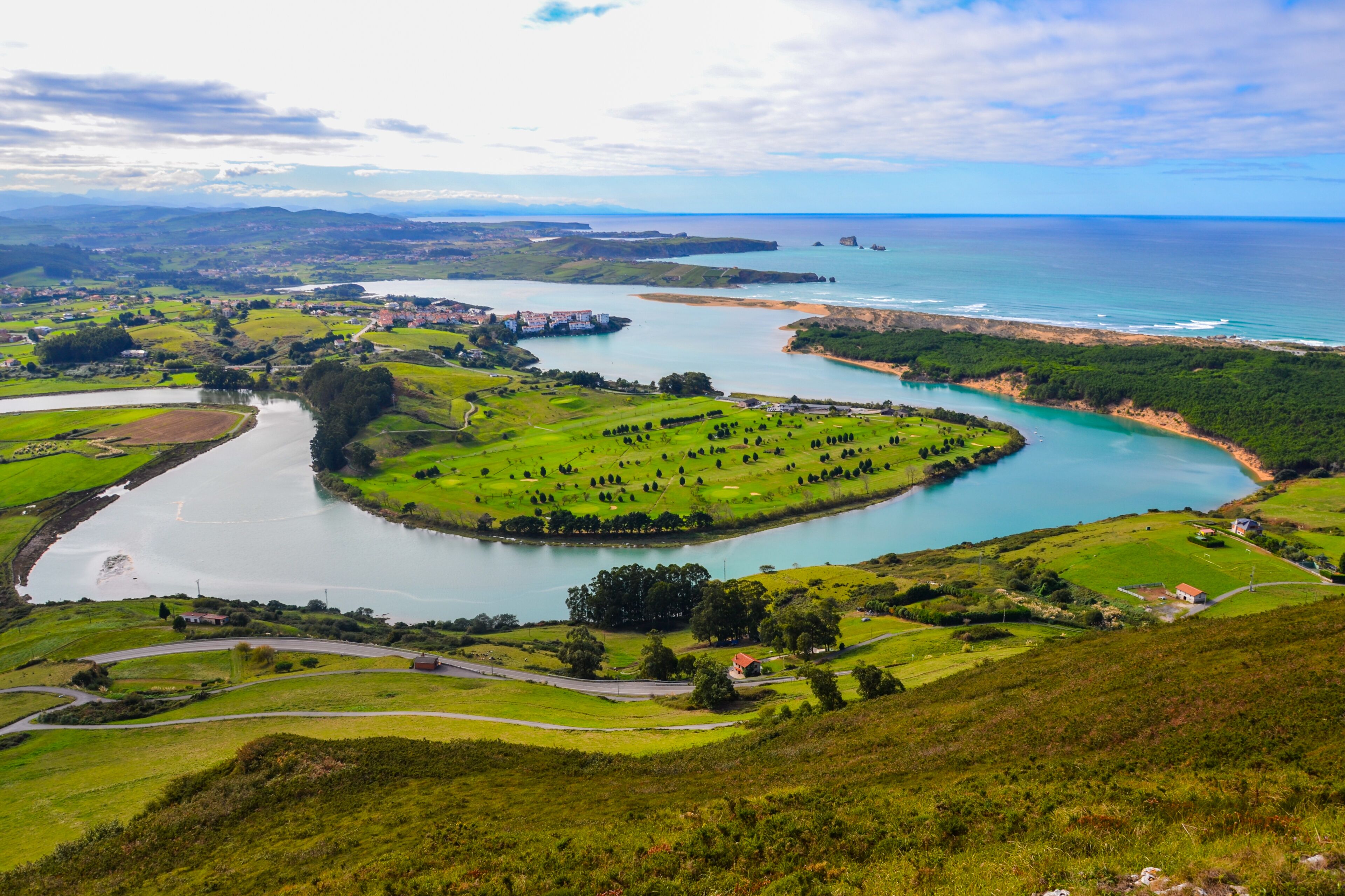 A coastal landscape with a river, green fields, and a small settlement.