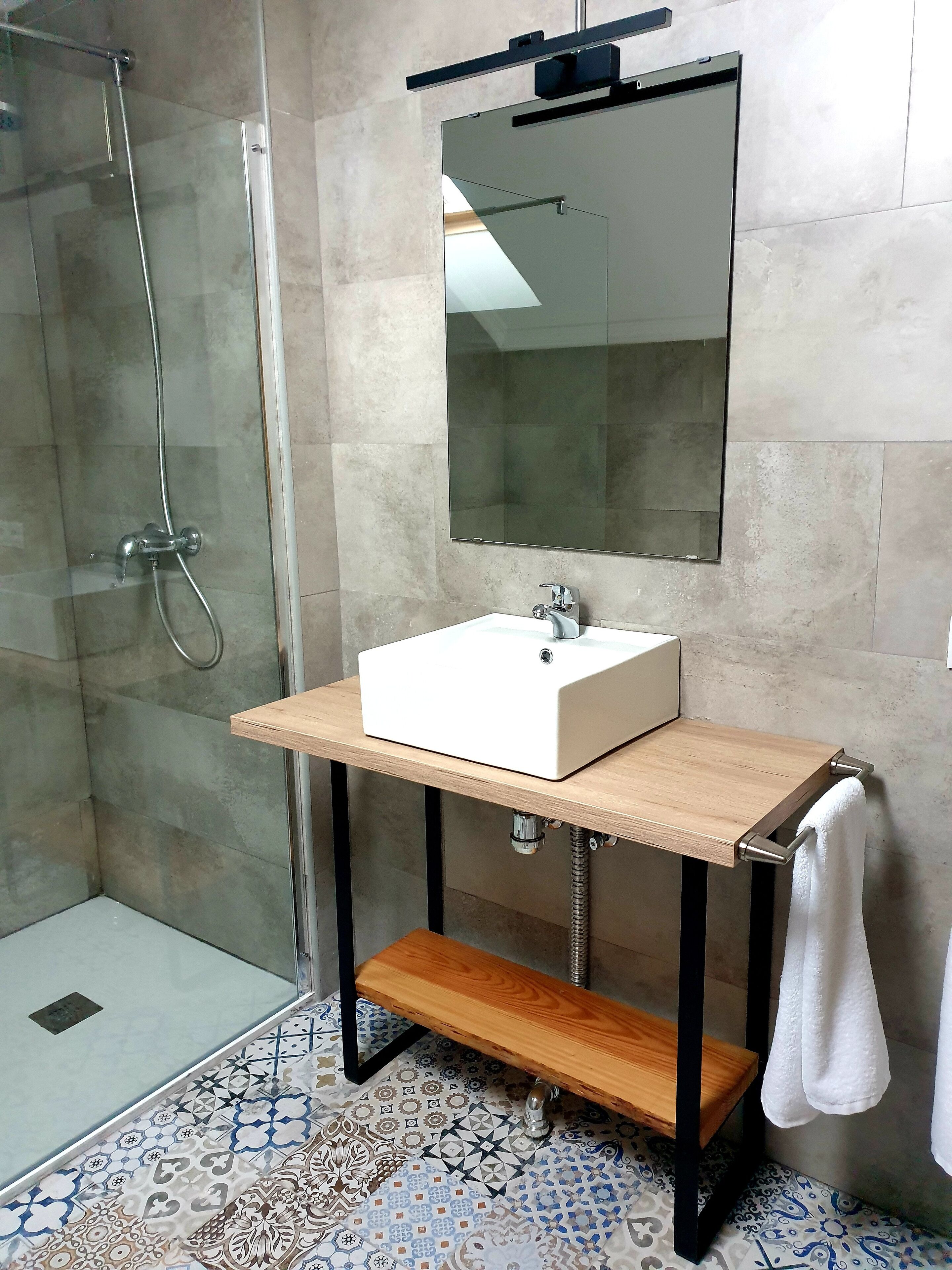 A modern bathroom with a glass shower enclosure, a white sink with a wooden countertop, and a mirror above it.
