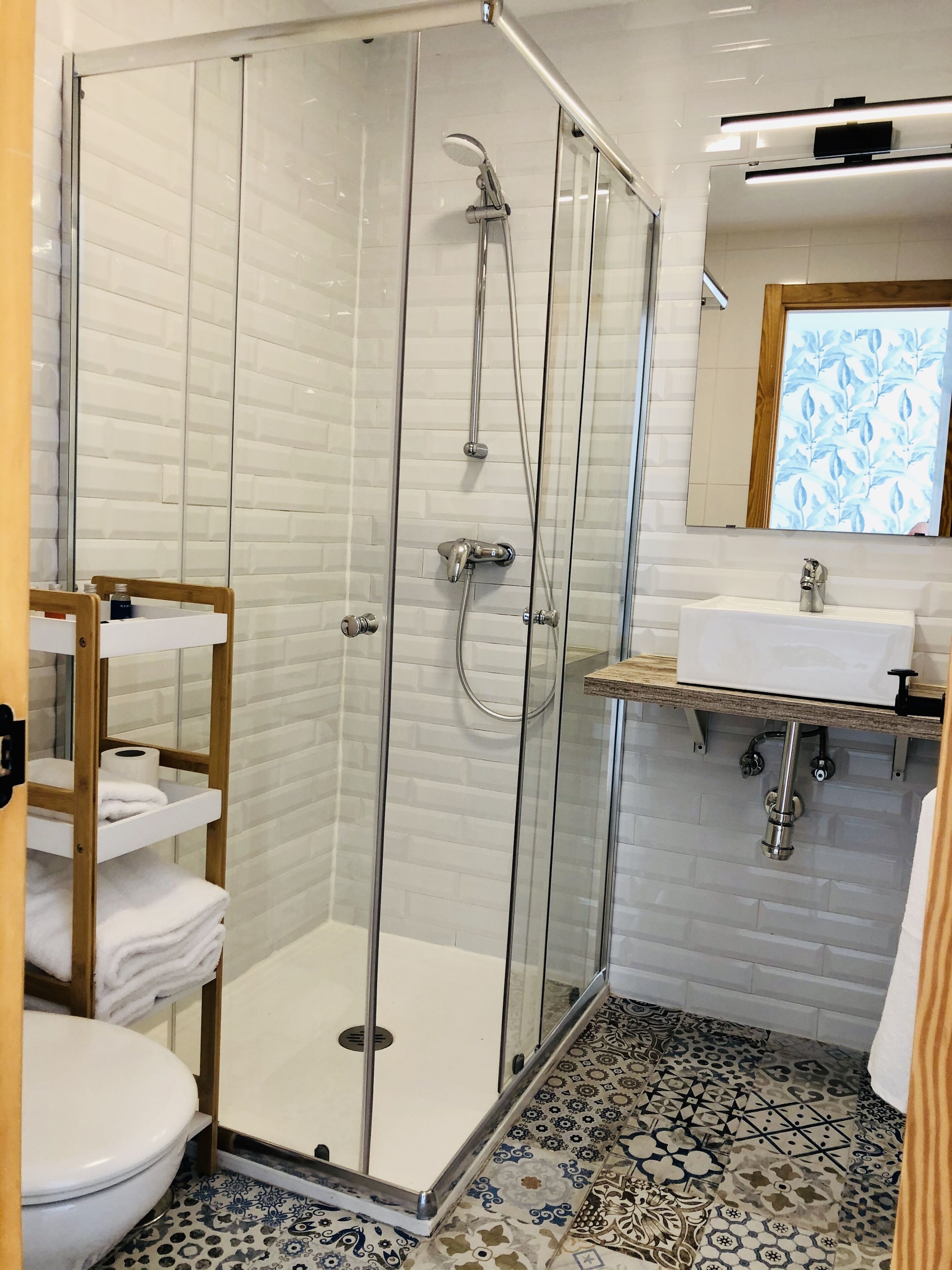 A modern bathroom with a glass-enclosed shower, a white sink, and a patterned floor.