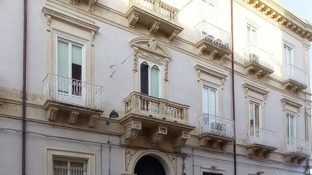 A historic building with a central entrance, multiple balconies, and a street in front. - Casa Cristina (Syracuse)