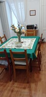 A dining area with a table covered by a green tablecloth, surrounded by wooden chairs. A vase with flowers is placed on the table.