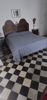 Un dormitorio con suelo a cuadros, colcha estampada, cabecero de madera, mesita de noche y lámpara.
