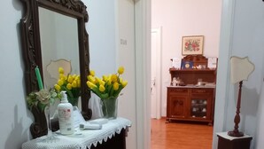 A hallway with a wooden floor, a mirror, a small table with a lace doily, a vase with yellow flowers, and a cabinet with drawers. - Casa Cristina (Syracuse)