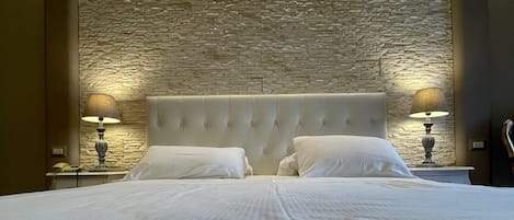 A bed with a textured stone wall behind it, two bedside lamps, and a tufted headboard.