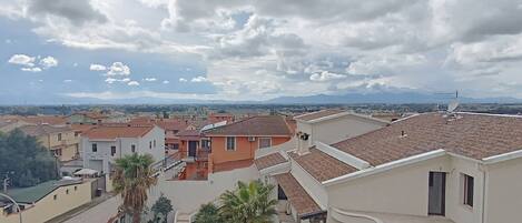 Zona residencial con casas, una calle y una cadena montañosa distante bajo un cielo nublado.