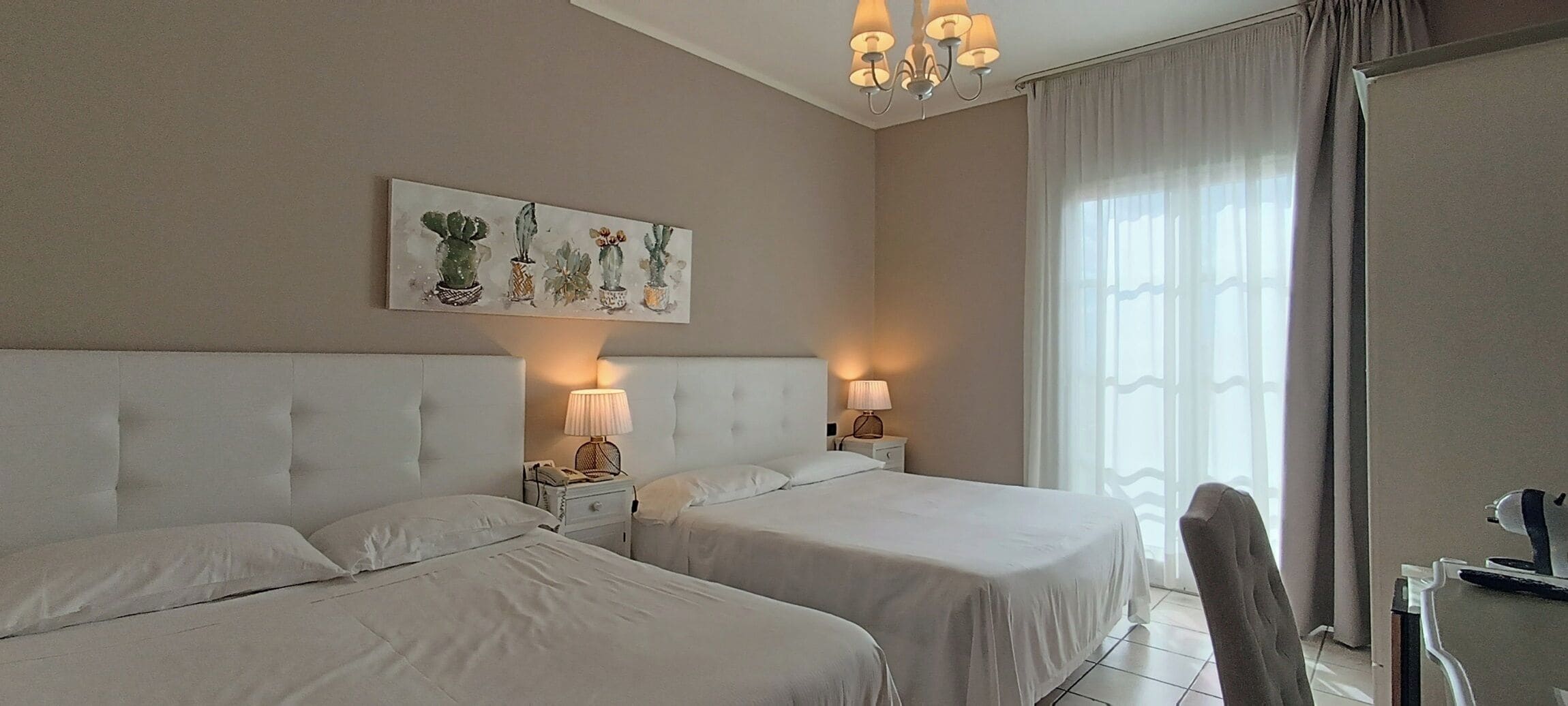 A hotel room with two beds, a chandelier, a painting, and a view of the outdoors.