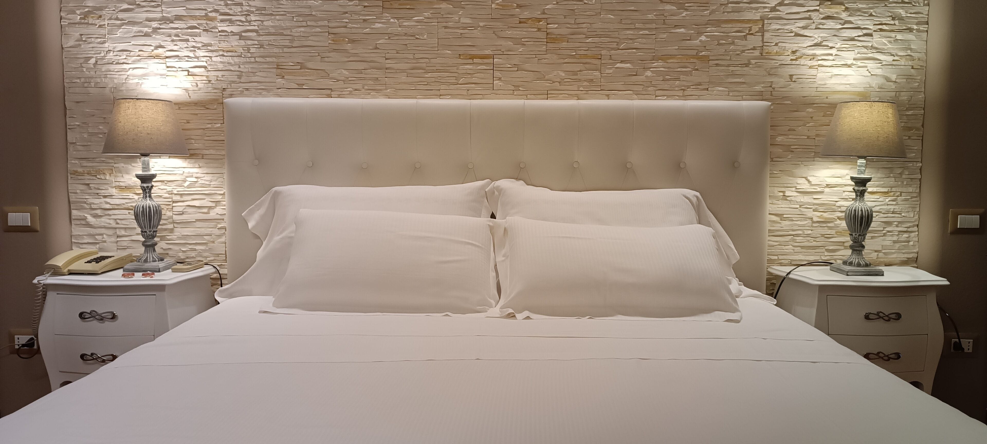 A bed with a tufted headboard, two bedside tables with lamps, and a stone-patterned wall behind.