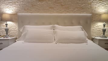 A bed with a tufted headboard, two bedside tables with lamps, and a stone-patterned wall behind.
