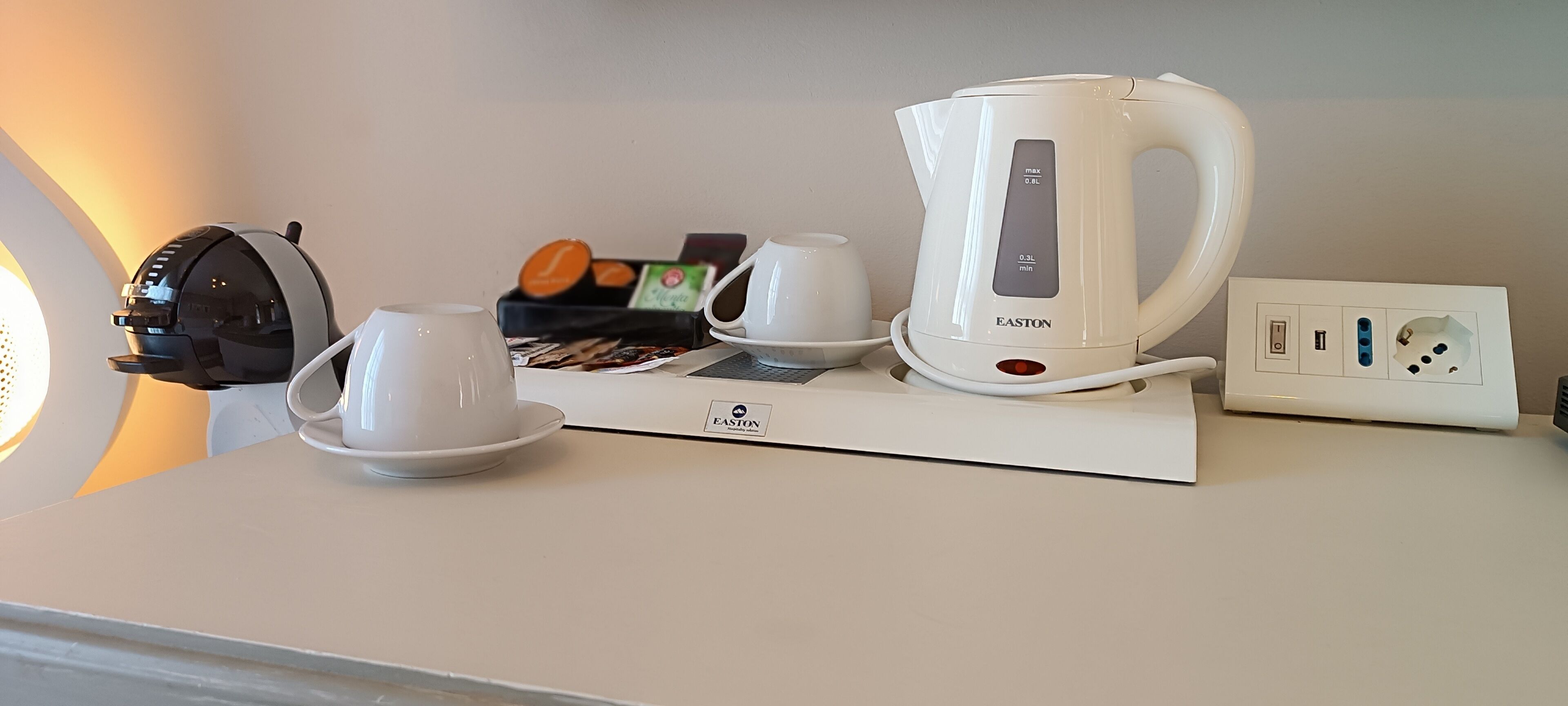 A kitchen counter with a coffee maker, two white cups, a kettle, and a box of tea bags.