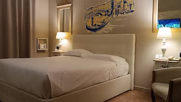 Habitación de hotel con una cama grande, dos lámparas de noche, una silla, una mesita de noche con un teléfono y un cuadro de un paisaje urbano veneciano.