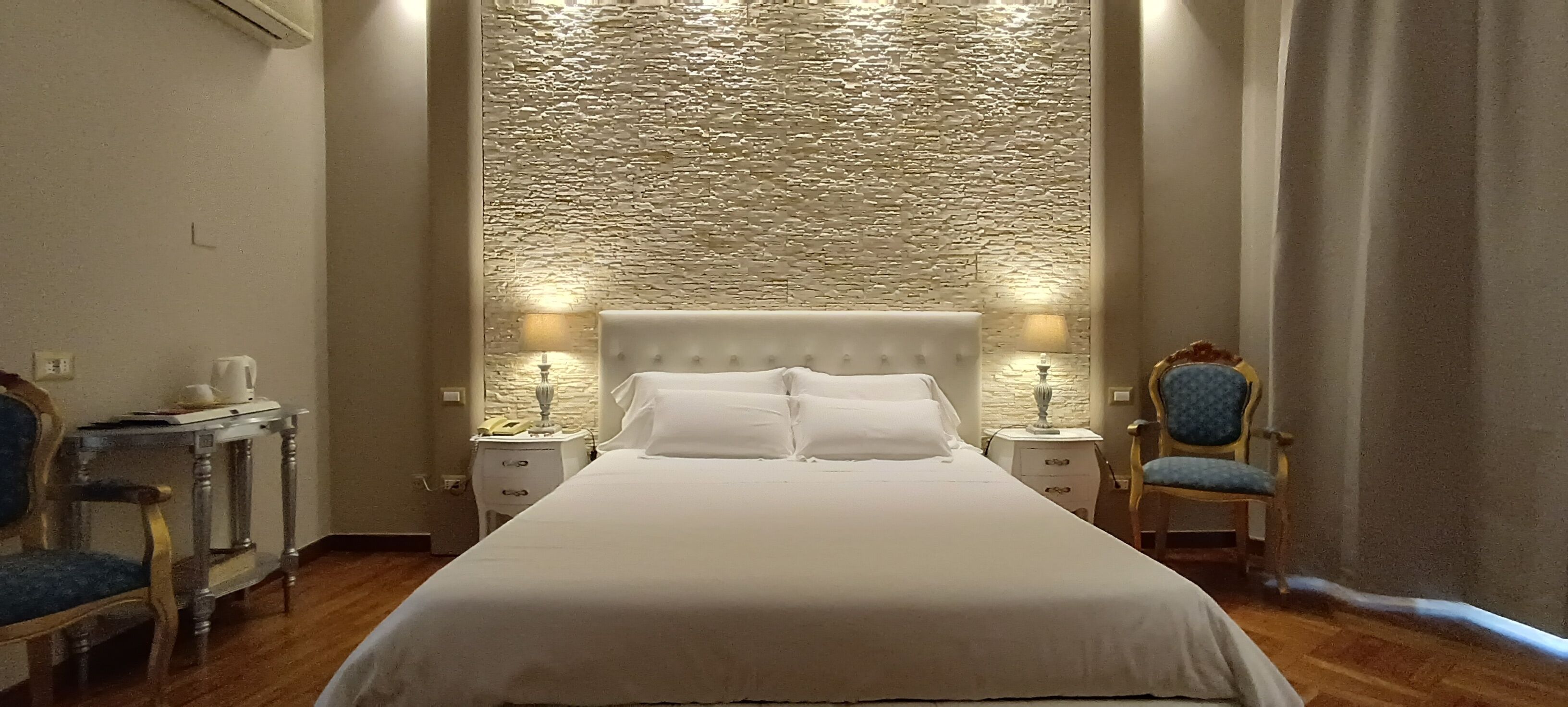 A hotel room with a large bed, two bedside tables, a chair, and a textured wall.