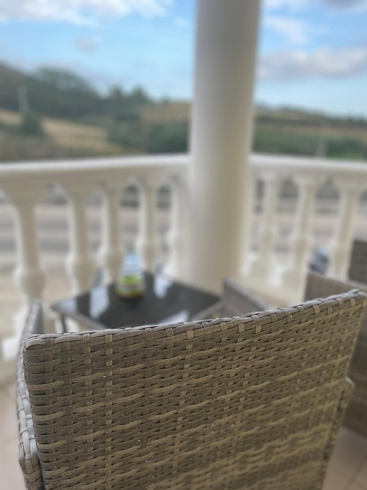 Una silla de mimbre con vistas a una barandilla blanca y una mesa con una botella encima.