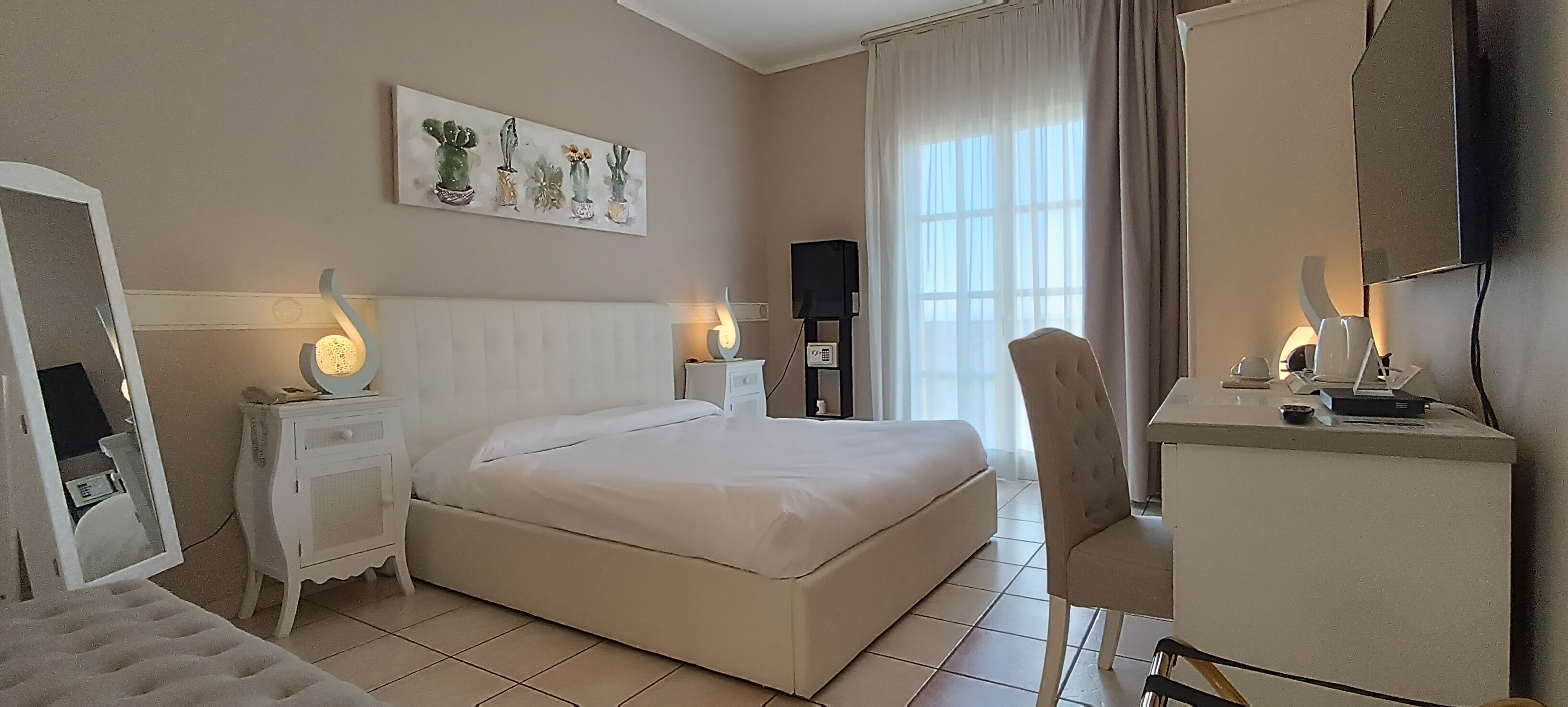 A hotel room with a bed, a desk, a chair, a TV, and a window with curtains.