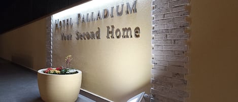 A wall with the text "HOTEL PALLADIUM Your Second Home" and a potted plant with flowers.