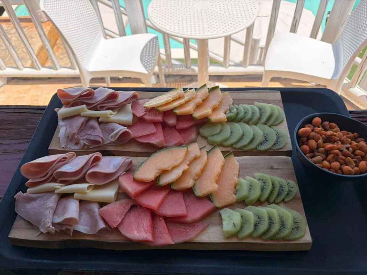 A wooden board with sliced meats, melon, and kiwi arranged on a tray.