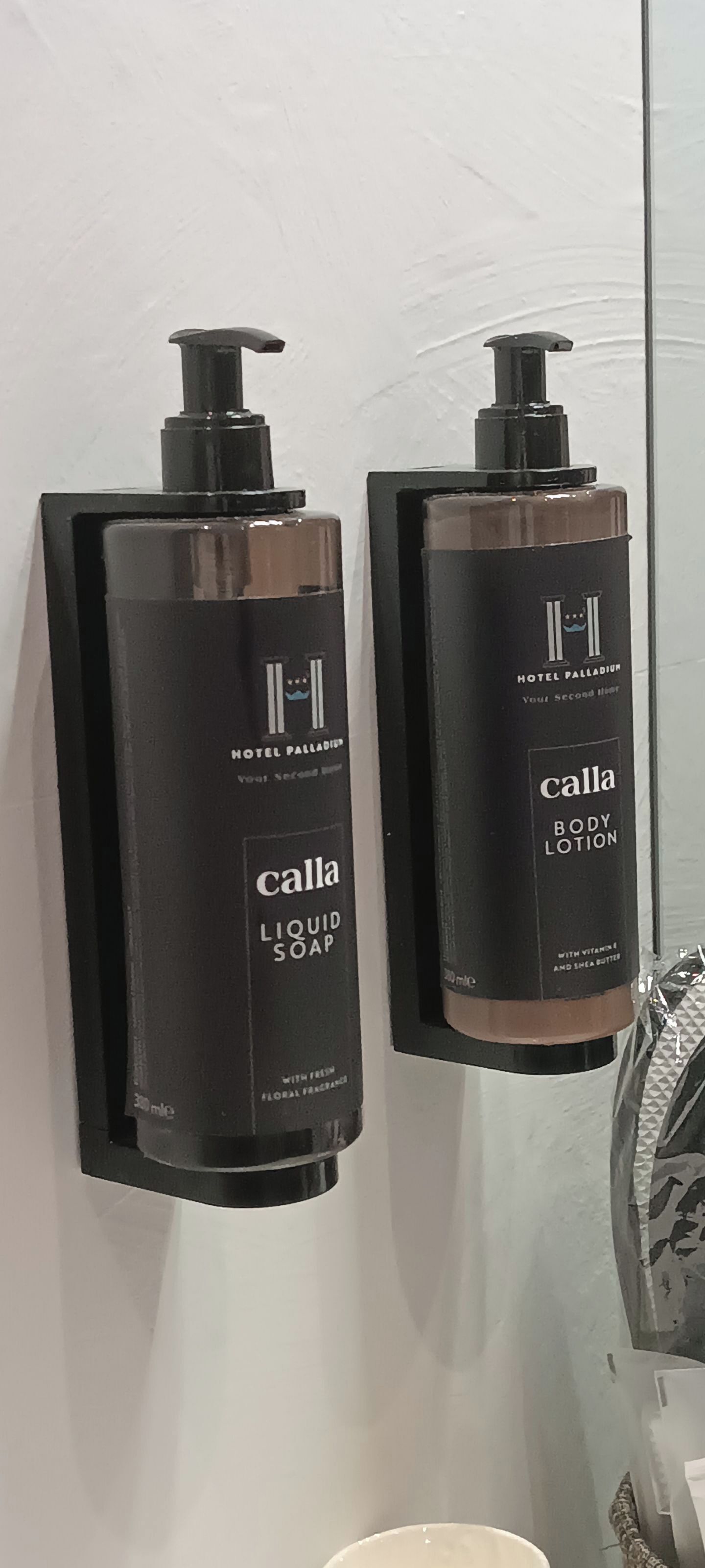 Two black wall-mounted dispensers of Calla body lotion and liquid soap.