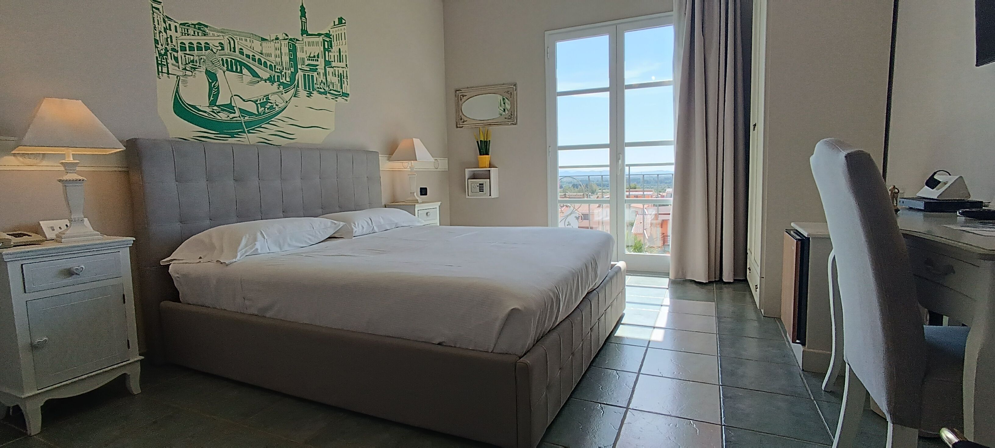Une chambre d’hôtel avec un grand lit, des tables de chevet, un bureau et une vue sur la ville par la fenêtre.
