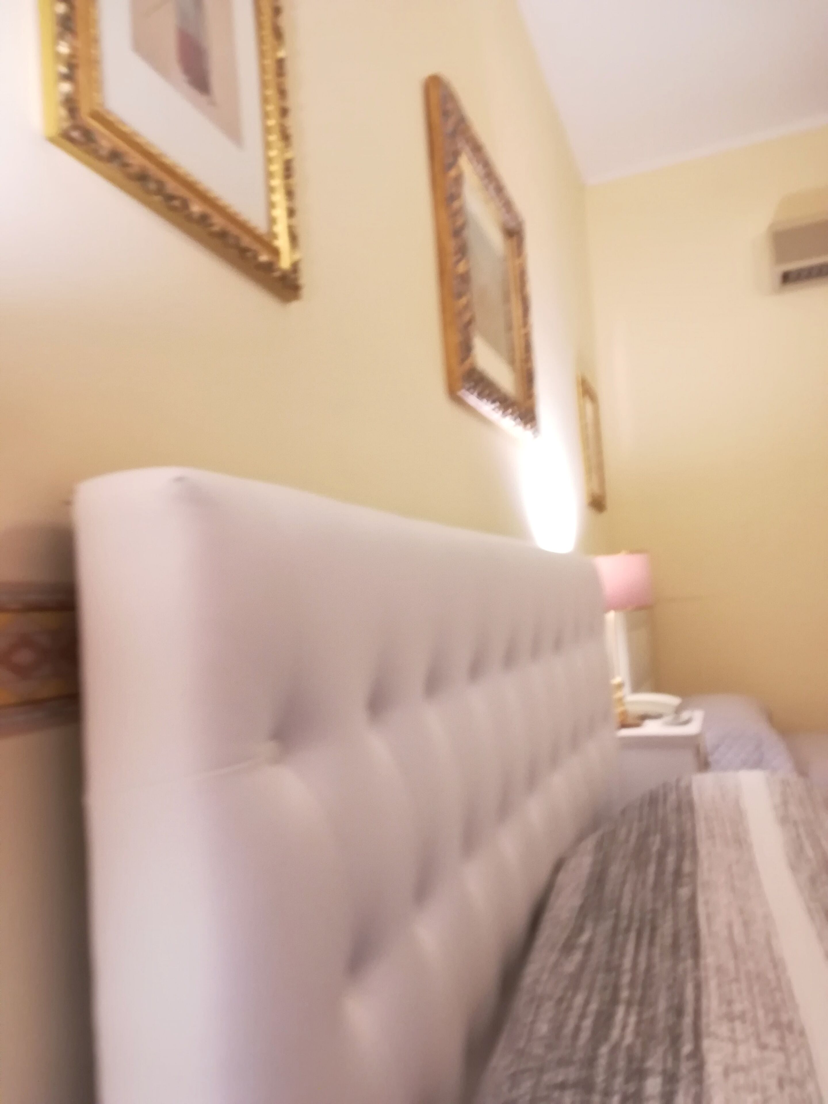 A bedroom with a tufted headboard, a bedside table with a lamp, and a bed with a patterned bedspread.