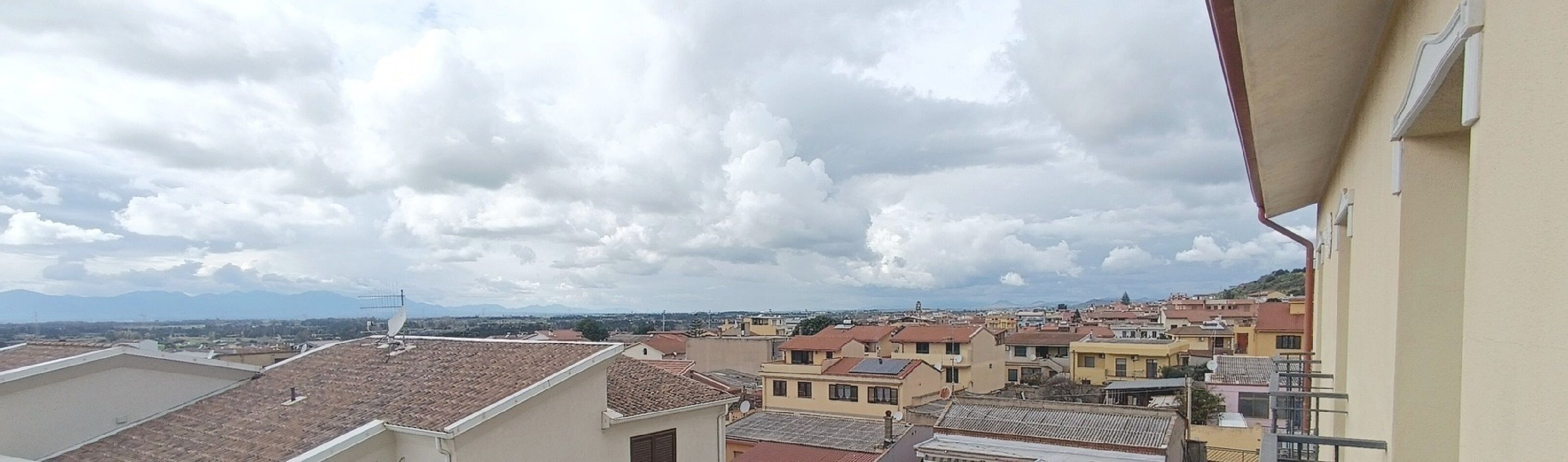 A residential area with terracotta-tiled roofs, a mix of building heights, and a mountainous backdrop.