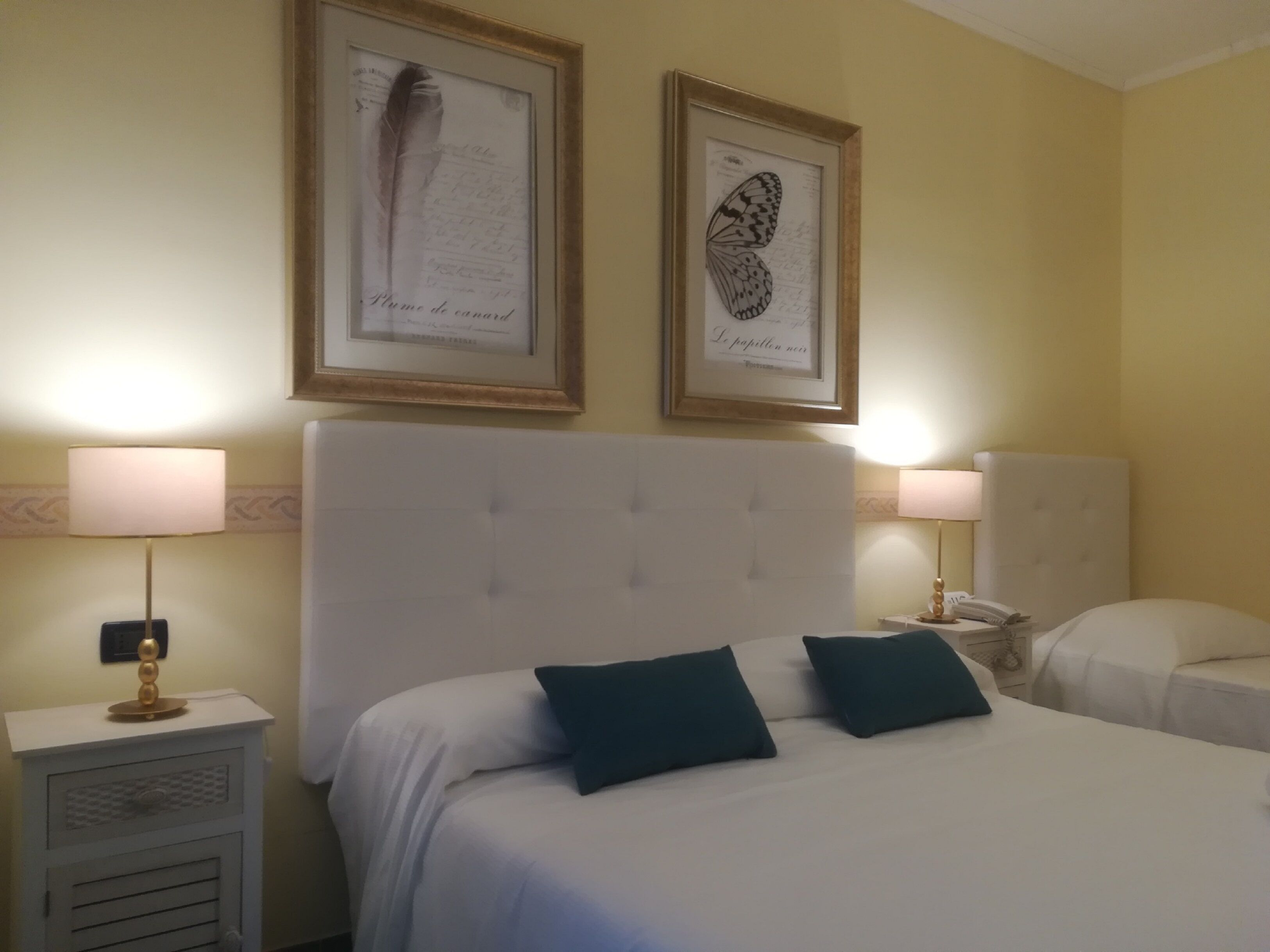 Une chambre d’hôtel avec un grand lit, deux lampes de chevet, une table de chevet et deux œuvres d’art encadrées accrochées au mur.