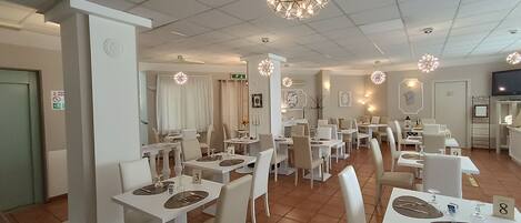 Un restaurante con mesas y sillas blancas, asientos numerados y luces esféricas decorativas en el techo.