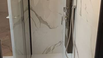 Ein modernes Badezimmer mit Duschkabine aus Glas, Marmorwänden und einer eleganten Duschbrause.