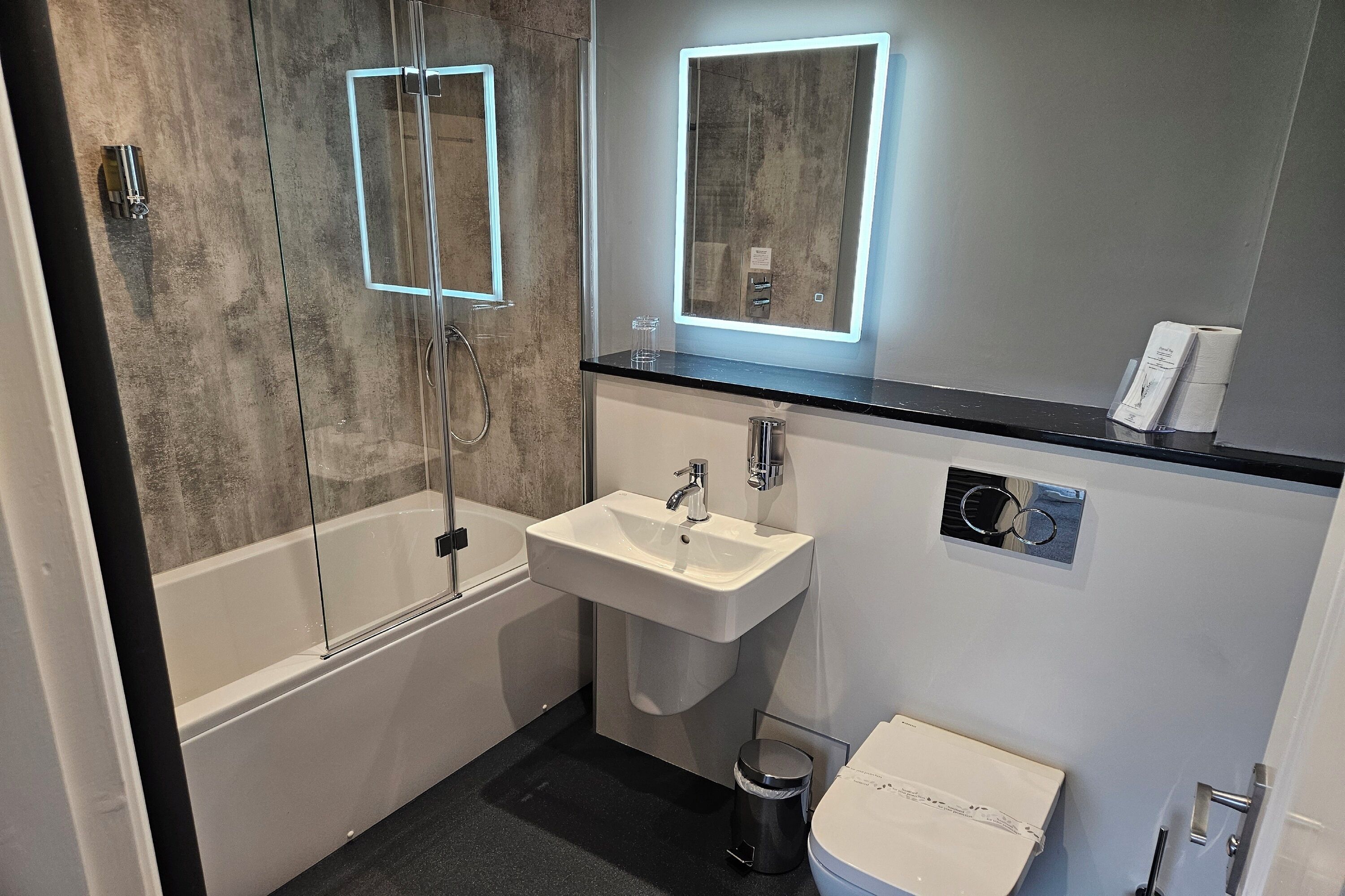 Un baño moderno con ducha de vidrio, lavamanos blanco y retrete.