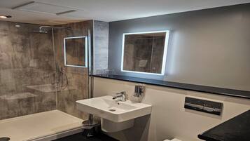A modern bathroom with a glass-enclosed shower, a white sink, and a mirror with integrated lighting.