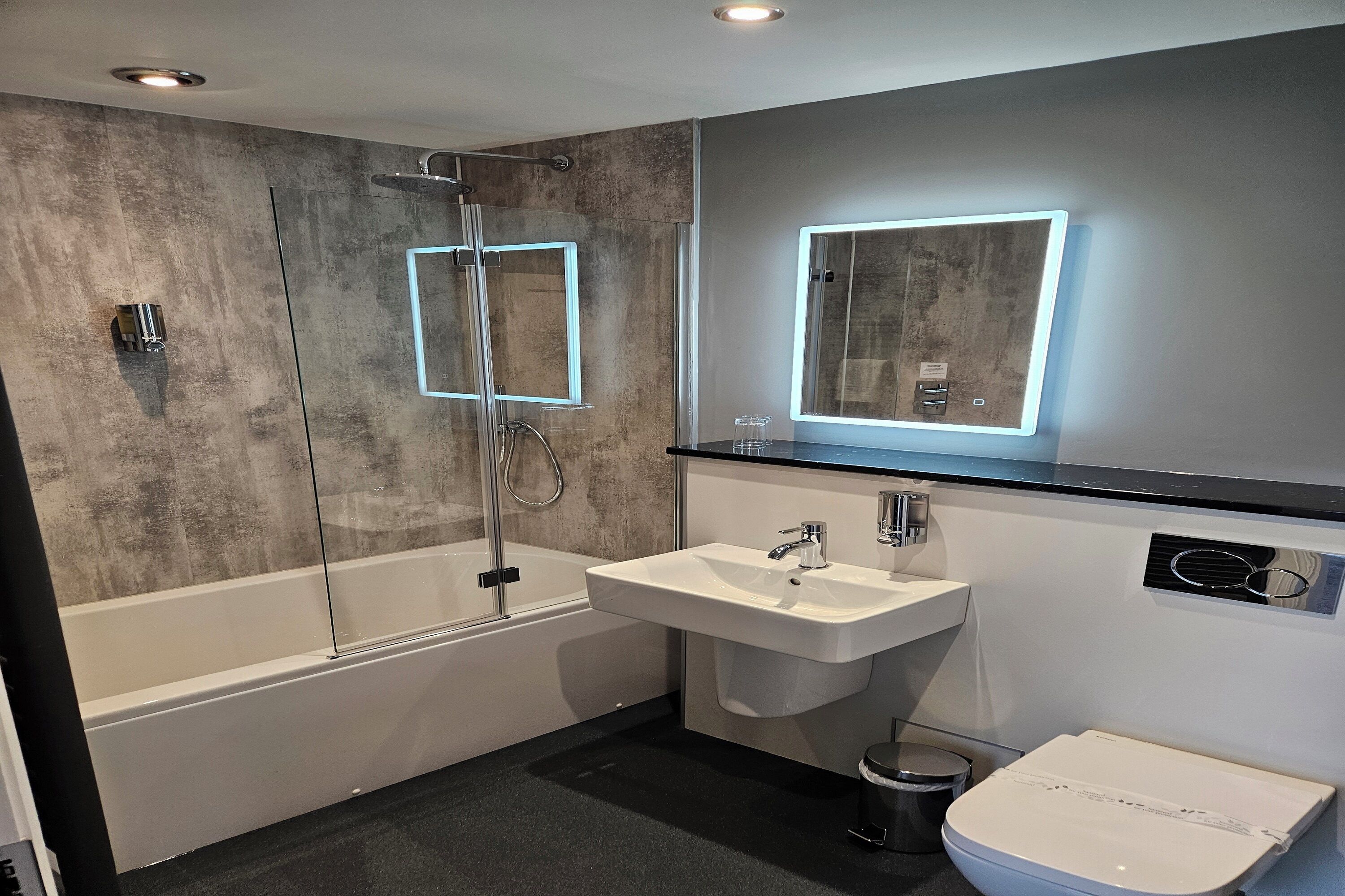 Ein modernes Badezimmer mit einer gläsernen Duschkabine, einem weißen Waschbecken und einer Toilette.