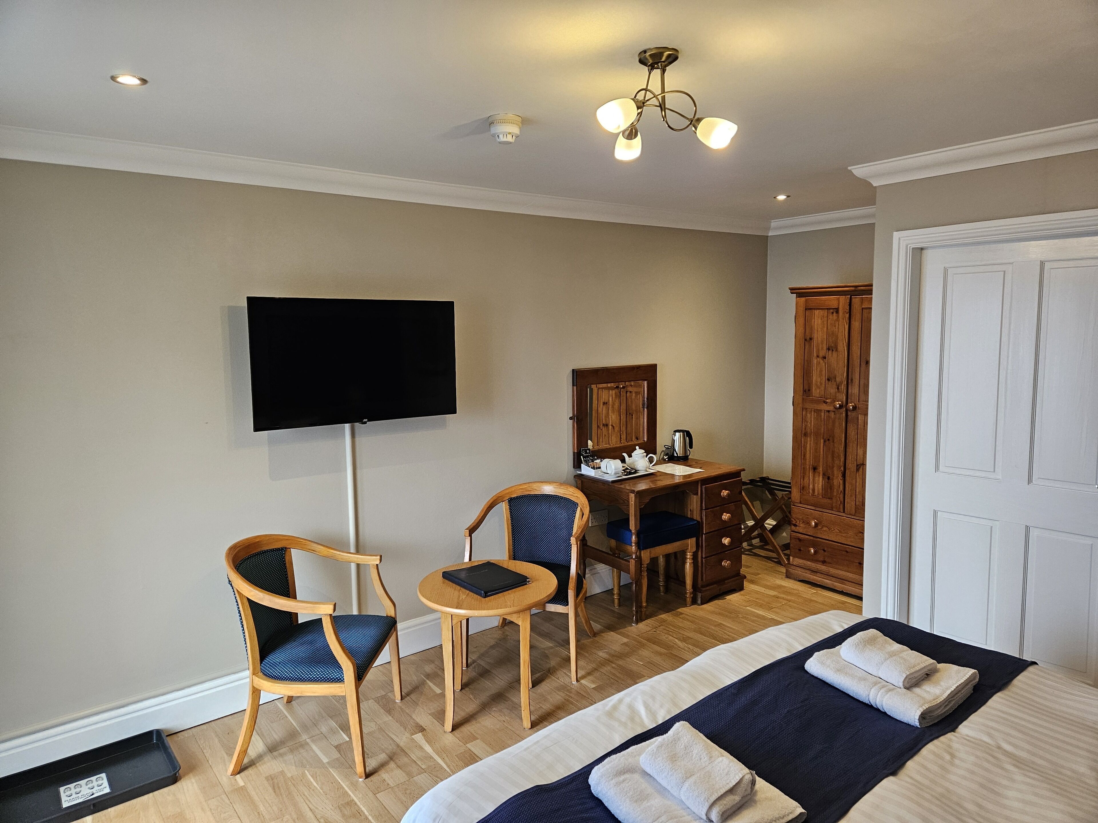 A hotel room with a bed, two chairs, a desk with a mirror, a television, and a wardrobe.
