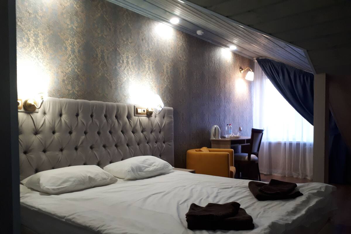 Hotellihuone, jossa on patjakuvioitu pääty ja sänky, työpöytä tuolilla sekä ikkuna, jossa on verhot.