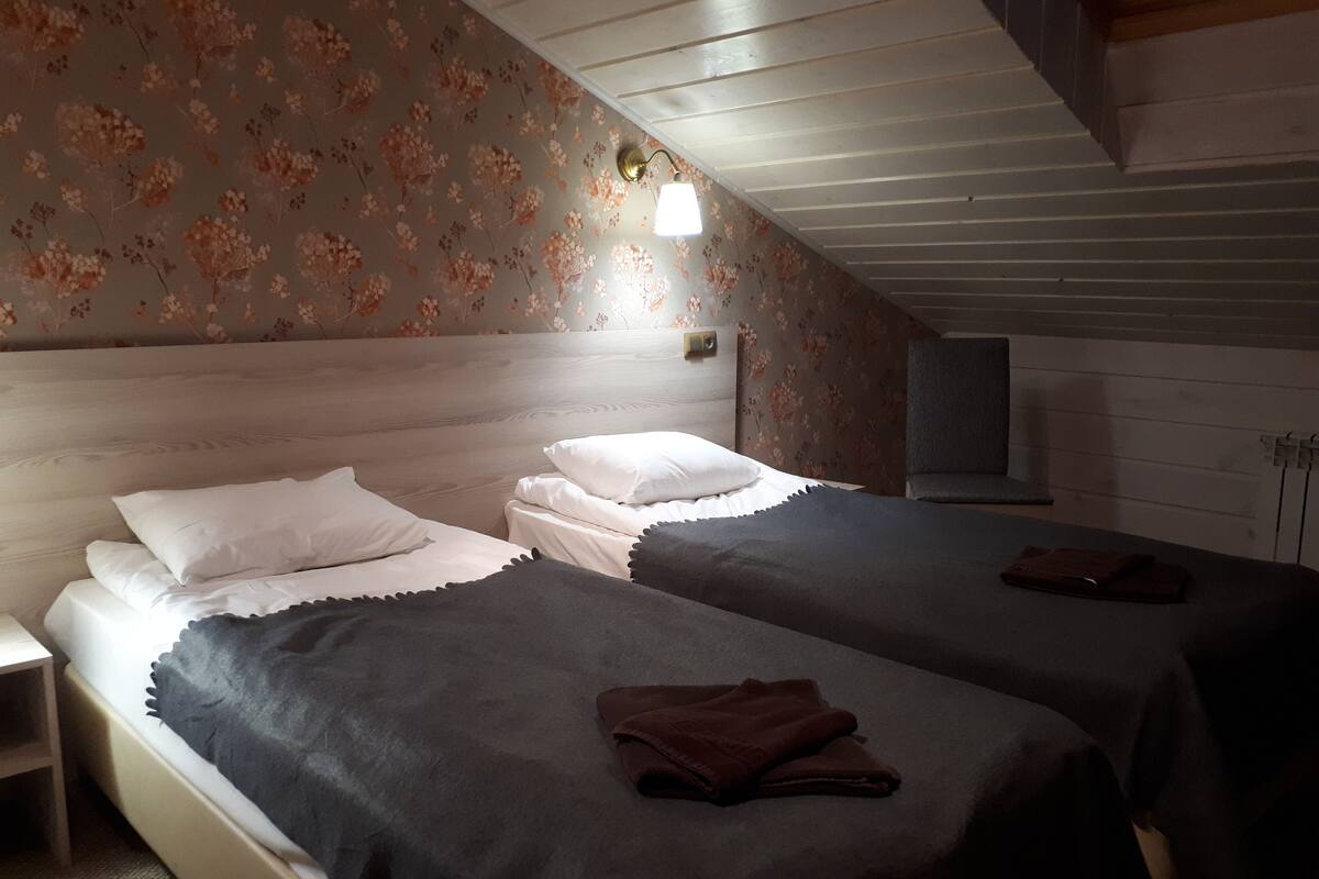 Makuuhuoneessa on kaksi sänkyä, puinen pääty ja yöpöytä sekä seinään kiinnitetty lamppu.