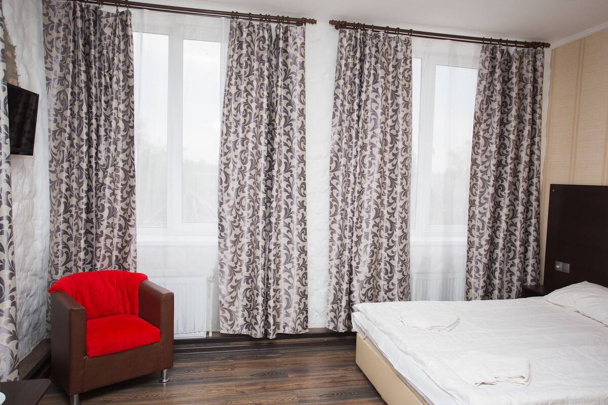 Hotellihuone, jossa on sänky, punainen tuoli ja kuviolliset verhot.