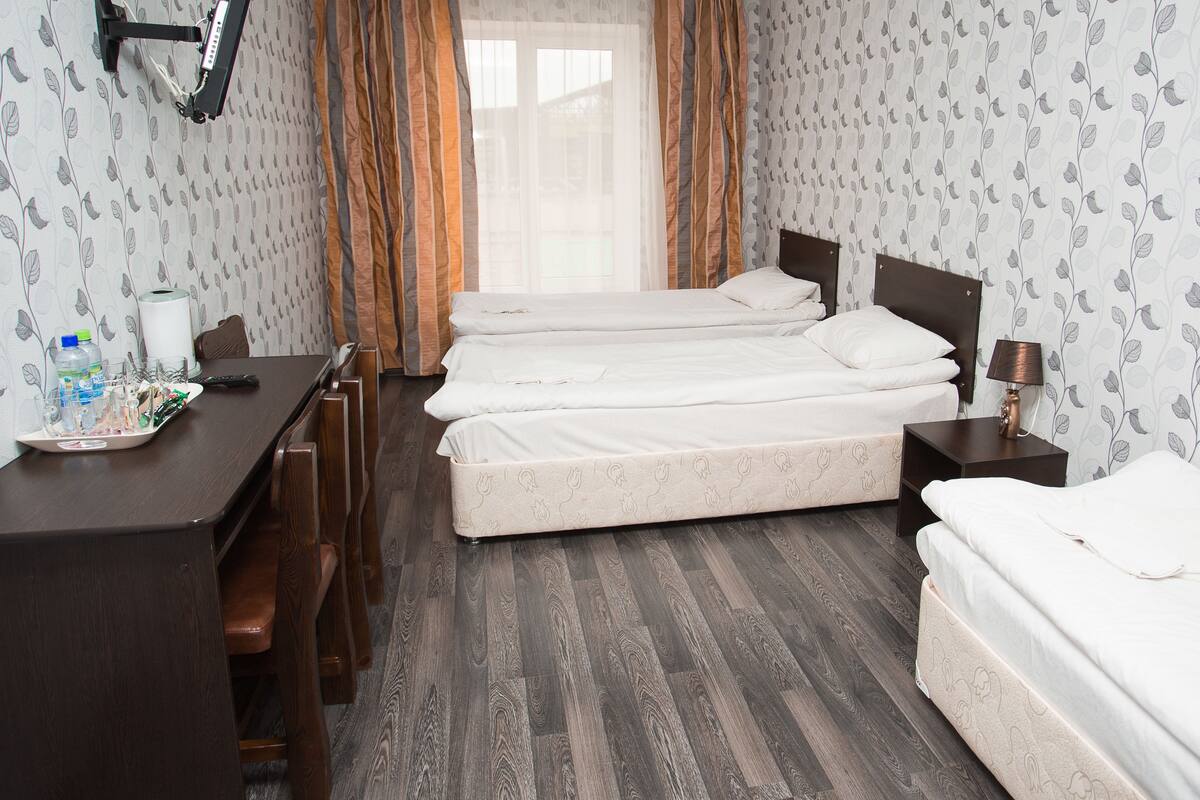 Hotellihuone, jossa on kaksi sänkyä, työpöytä, tuoleja, lamppu ja ikkuna, jossa on verhot.