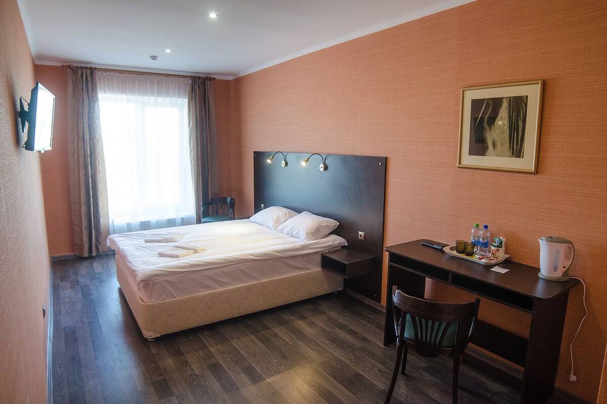 Hotellihuone, jossa on sänky, työpöytä, tuoli ja taulu seinällä.