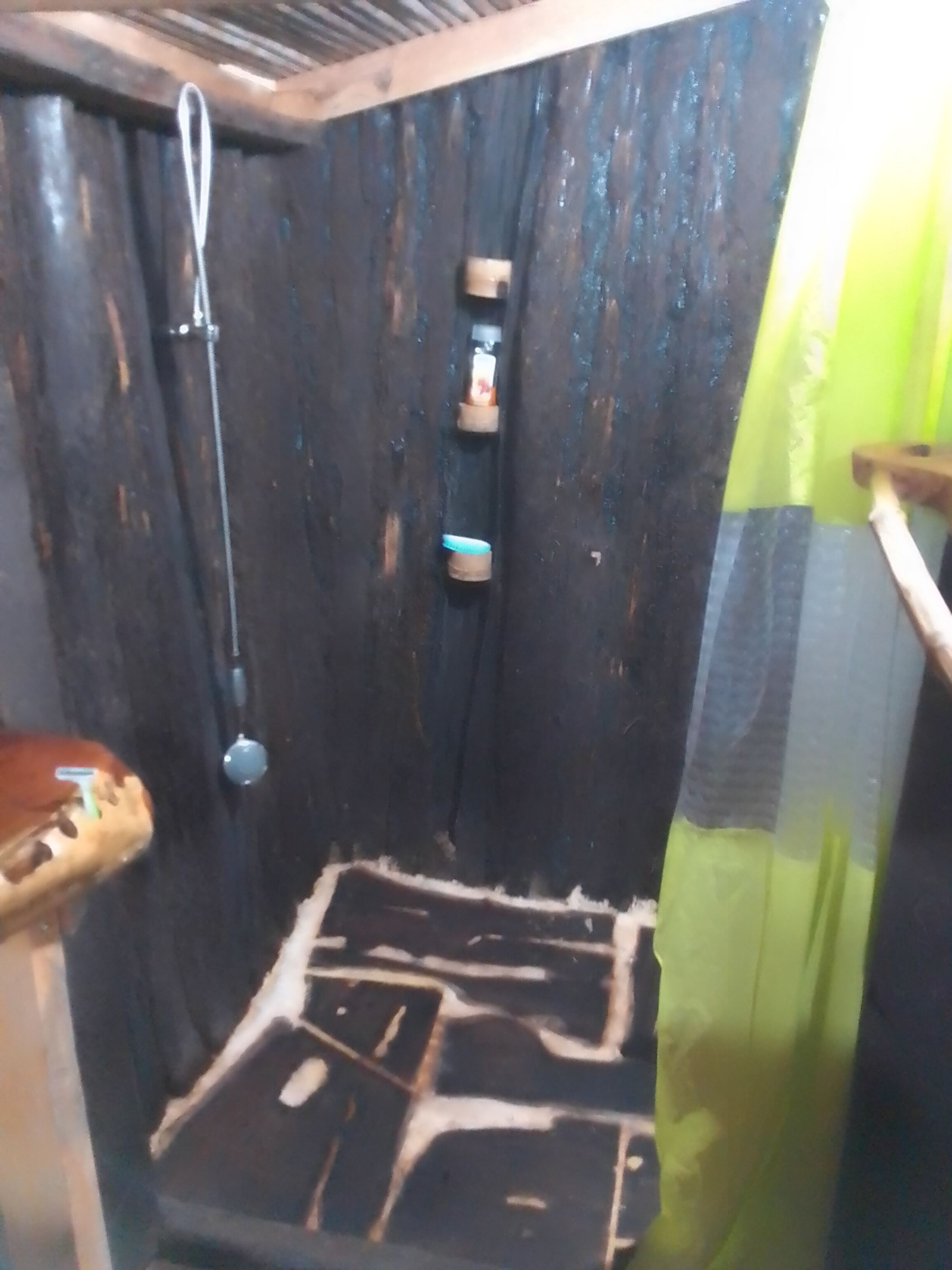 Une salle de bain avec une douche, des toilettes et un lavabo. Les murs sont en bois et il y a un rideau vert.