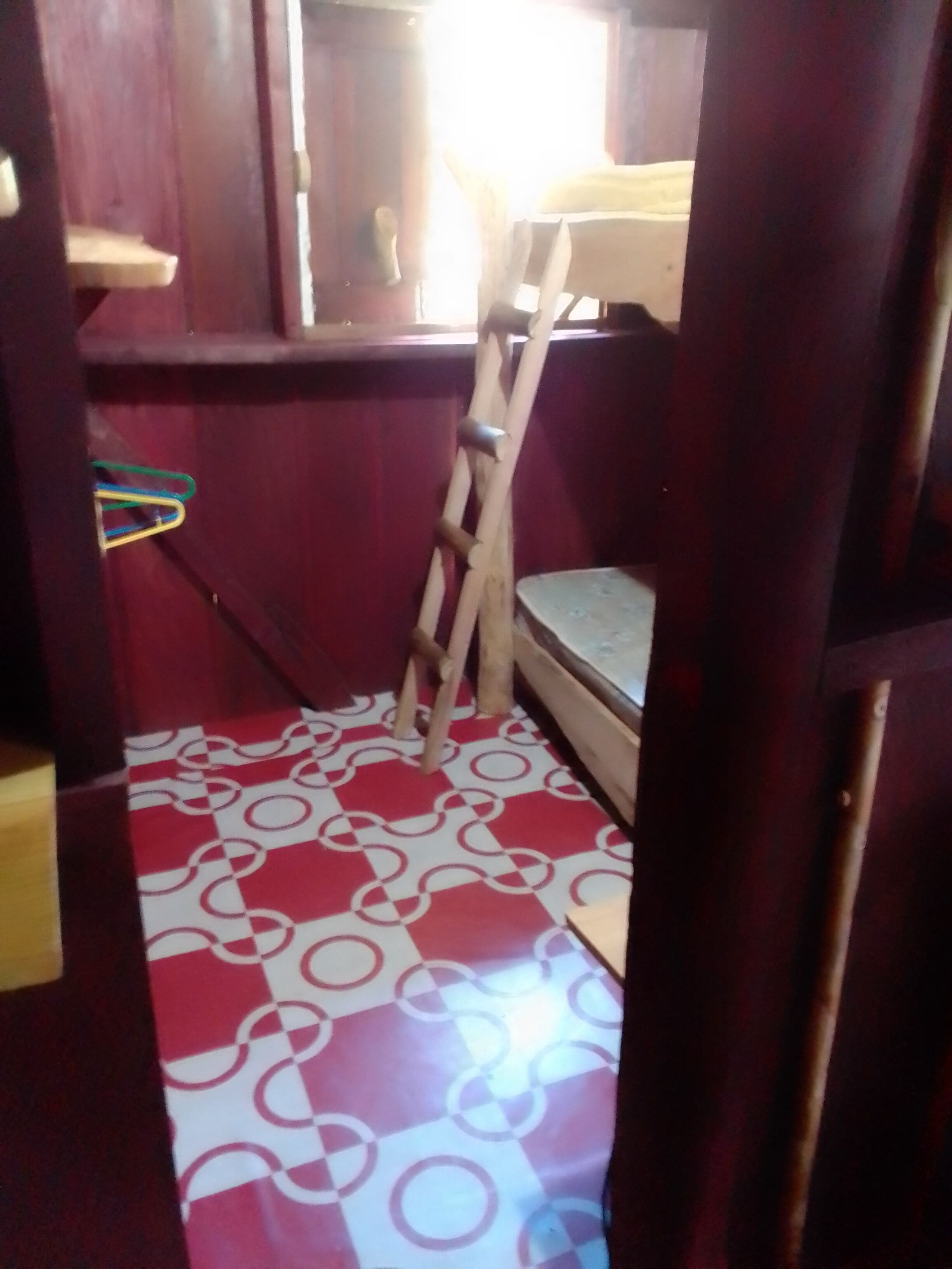 Una habitación con piso de estampado rojo y blanco, una escalera de madera y una cama litera.