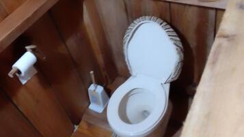A wooden cabin-style bathroom with a toilet, a roll of toilet paper, and a toilet brush.