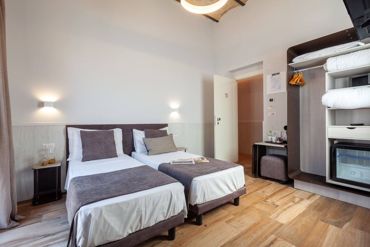 A hotel room with two beds, a wardrobe, a minibar, and a door to another room.