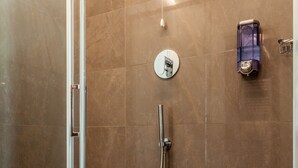 Un área de ducha moderna con puerta de vidrio, suelo de madera y un cabezal de ducha instalado en la pared.