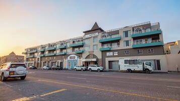 Un hotel de varios pisos con techo plano, varios balcones y un estacionamiento con varios coches.