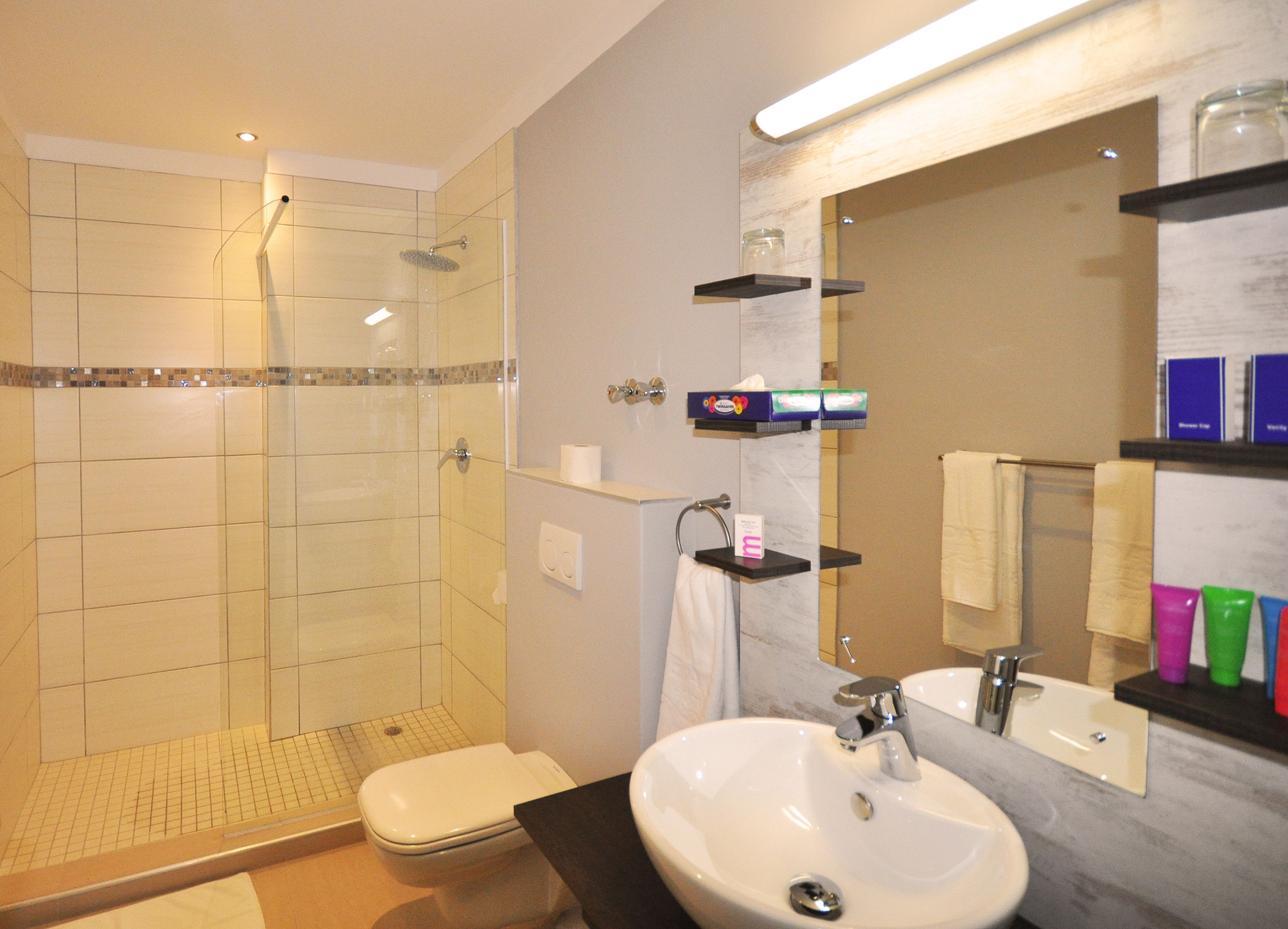 A modern bathroom with a glass-enclosed shower, a white toilet, a sink with a mirror, and shelves with toiletries.