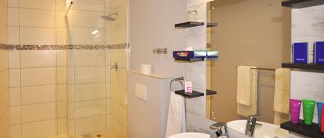 A modern bathroom with a glass-enclosed shower, a white toilet, a sink with a mirror, and shelves with toiletries.
