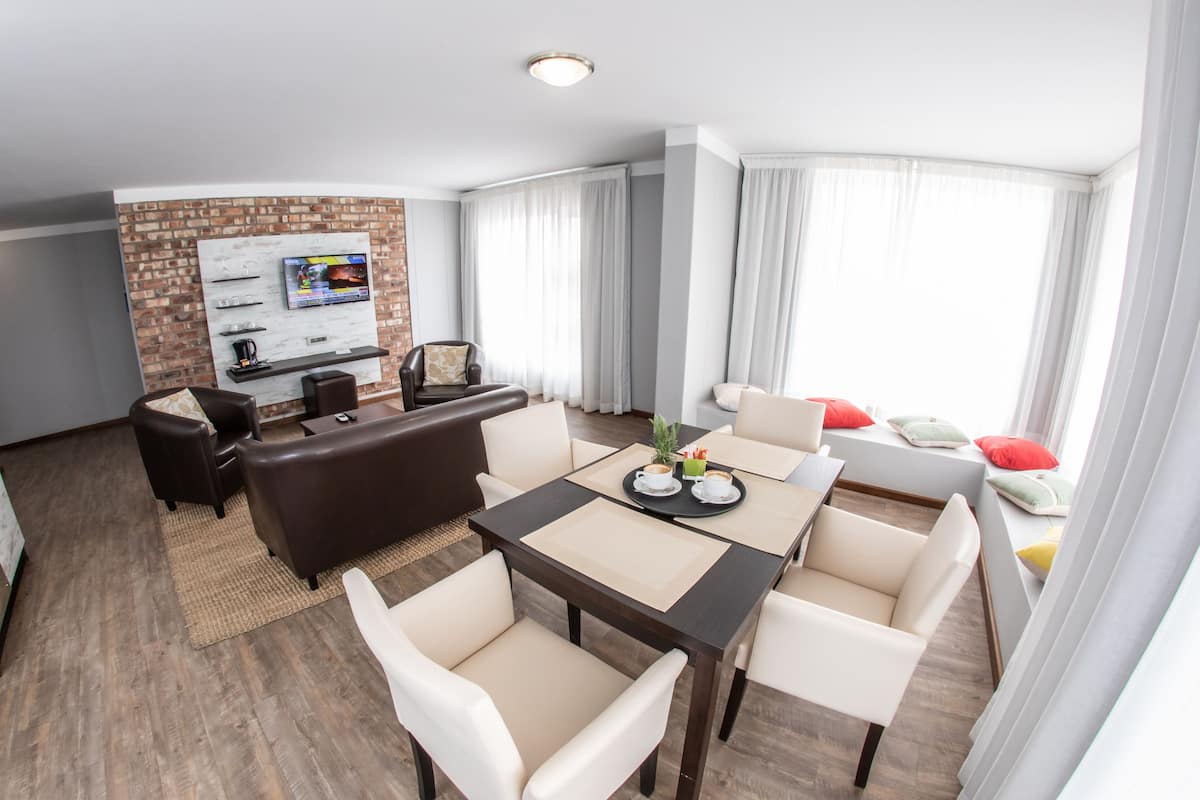 A modern living room with a fireplace, a TV mounted on a brick wall, and a dining area with a table and chairs.