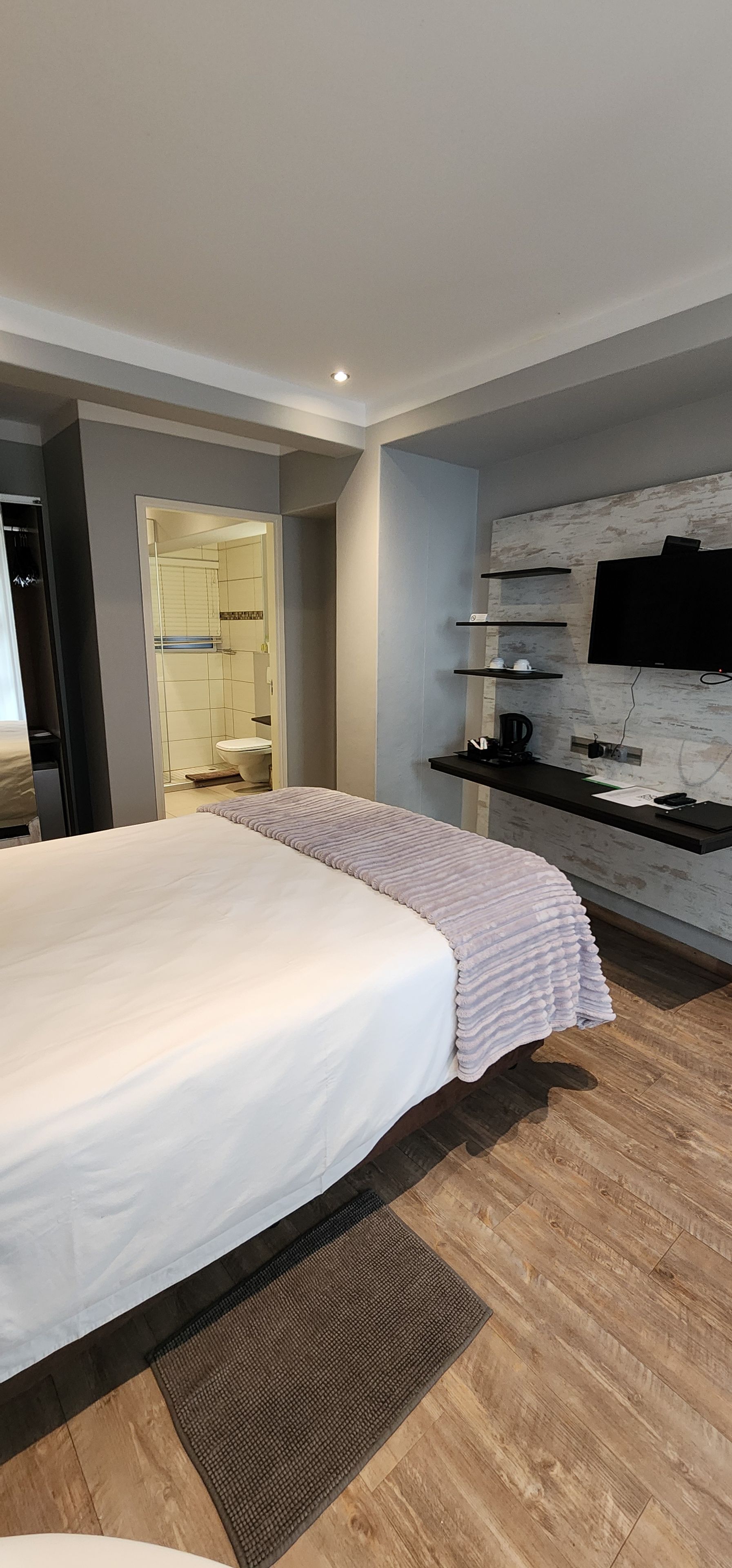 Quarto moderno com cama grande, TV integrada e área de chuveiro.