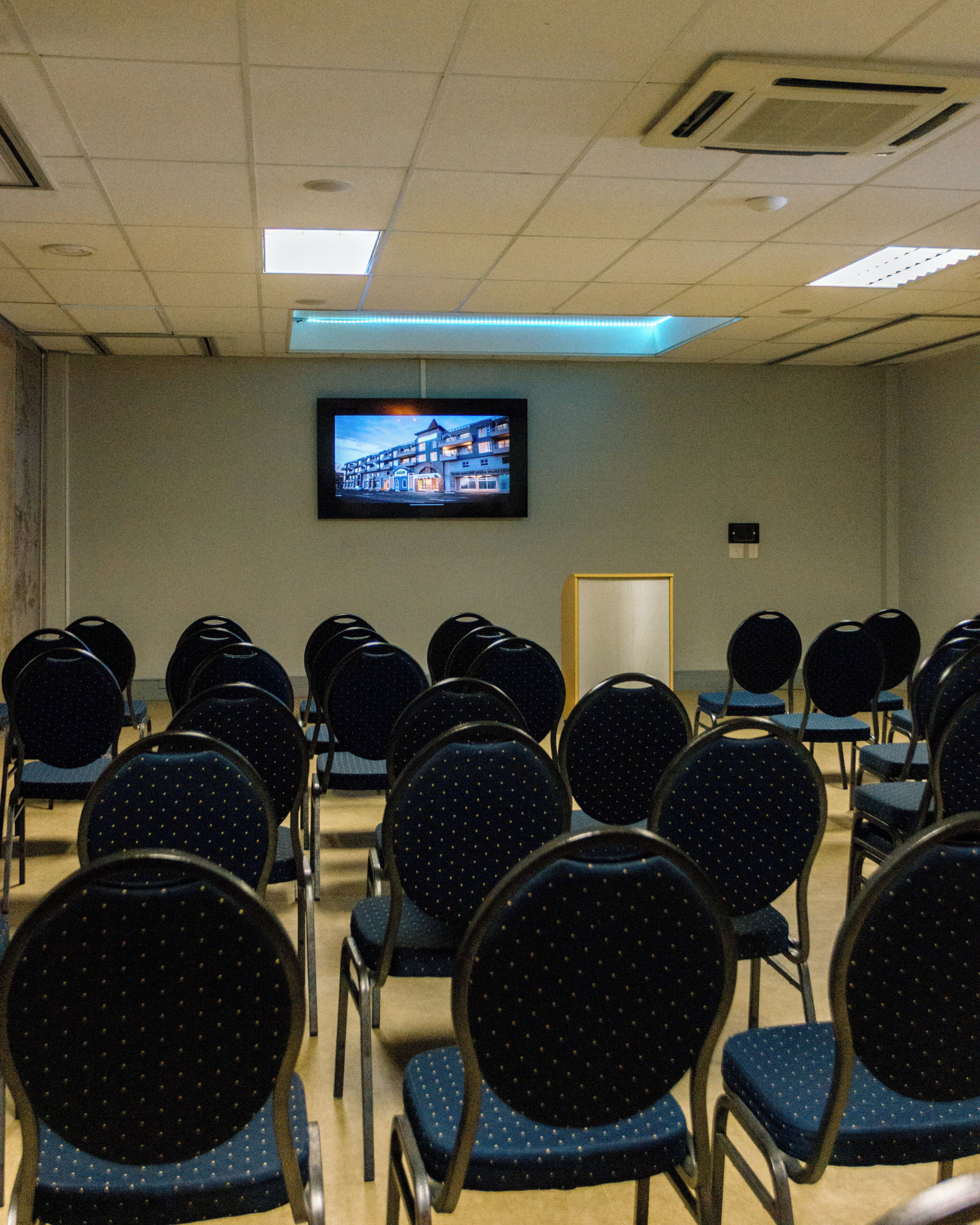 A conference room with rows of chairs, a television screen on the wall, and a door.