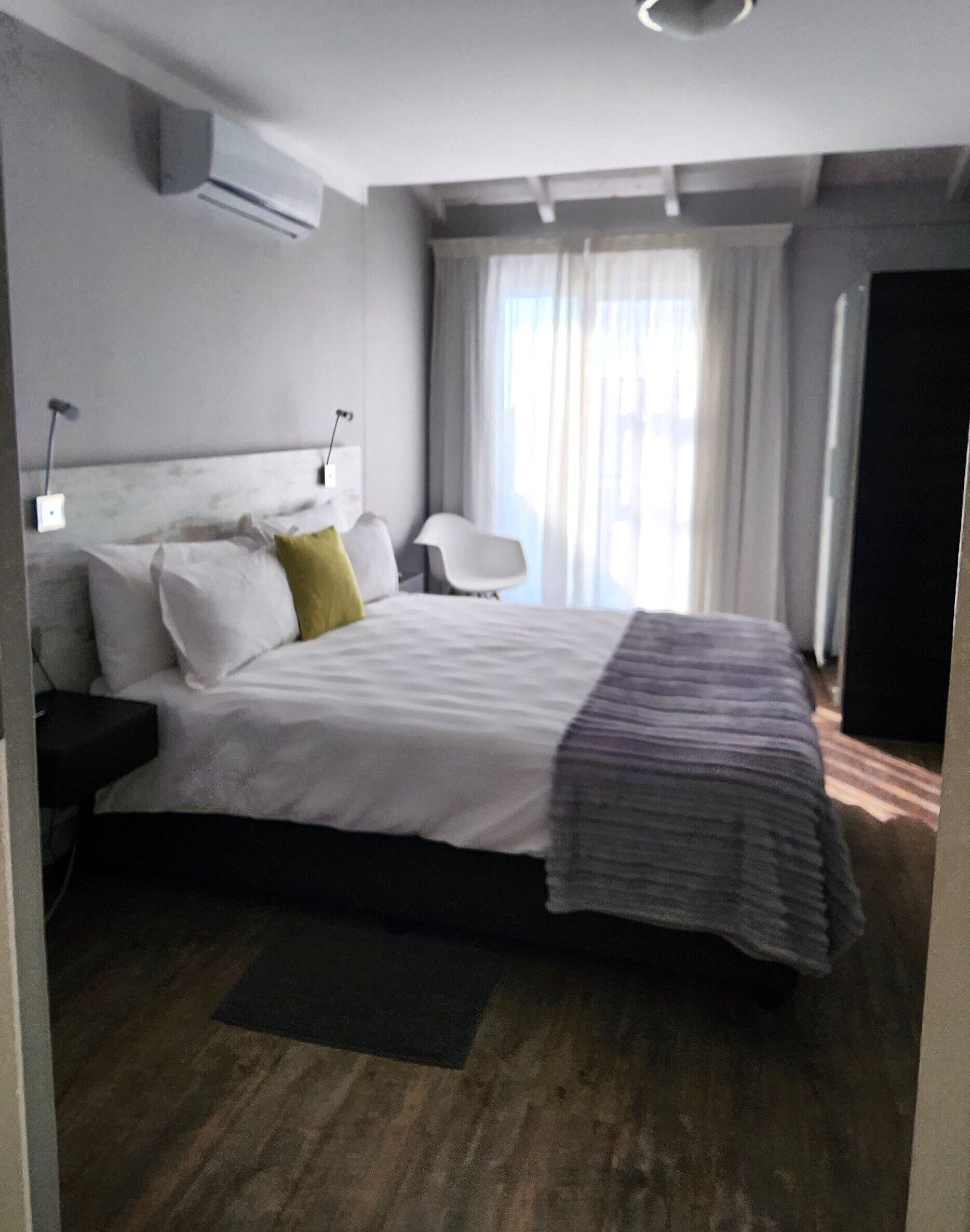 Una habitación de hotel moderna con una cama grande, una mesita de noche, una silla y un ventanal con cortinas.
